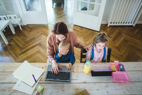 Hohe Winkel Ansicht der Mutter arbeitet am Laptop, während mit niedlichen Sohn von Tochter mit digitalen Tablet am Tisch sitzen - MASF14602
