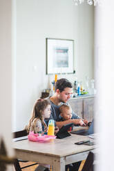 Vater benutzt Laptop, während er mit süßen Kindern am Tisch sitzt - MASF14603