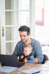 Man working on laptop while sitting with son at table - MASF14606