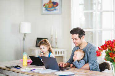 Mittlerer erwachsener Mann, der am Laptop arbeitet, während er mit Kindern am Tisch sitzt - MASF14609