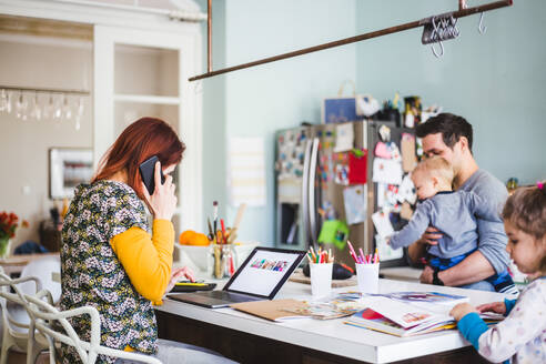 Woman working on laptop while sitting with family in kitchen at home - MASF14612