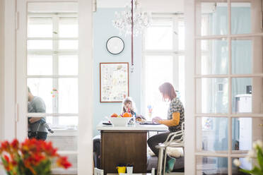 Woman working on laptop while sitting with girl in kitchen at home - MASF14615