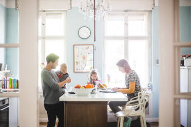 Vater spielt mit seinem Sohn und steht neben einem Mädchen und einer Frau, die an der Kücheninsel beschäftigt ist - MASF14616