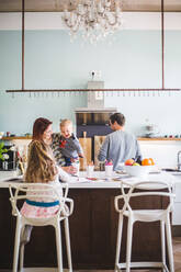 Frau sieht ihren Sohn an, während sie neben ihrer Tochter steht und in der Küche lernt - MASF14620