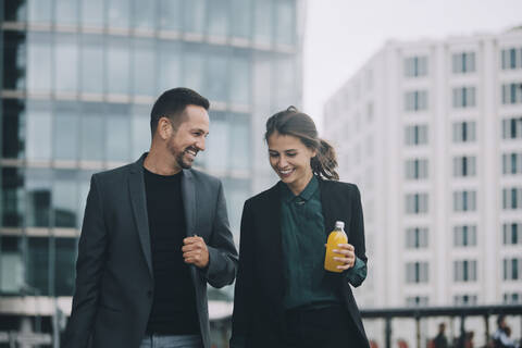 Lächelnde Geschäftsfrau und Geschäftsmann im Gespräch beim Spaziergang in der Stadt, lizenzfreies Stockfoto