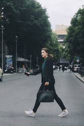 Seitenansicht einer Geschäftsfrau beim Überqueren der Straße in der Stadt - MASF14643