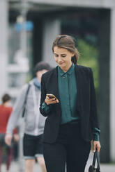 Selbstbewusste Geschäftsfrau, die ein Smartphone benutzt, während sie auf der Straße in der Stadt spazieren geht - MASF14649