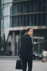 Geschäftsfrau schaut über die Schulter beim Gehen auf der Straße in der Stadt - MASF14650