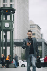 Älterer Geschäftsmann, der ein Mobiltelefon benutzt, während er in der Stadt auf der Straße geht - MASF14655