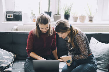 High angle view of female colleagues discussing over laptop while sitting in creative office - MASF14663