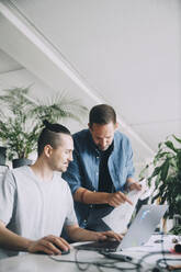 Creative businessmen discussing over document at desk in office - MASF14679