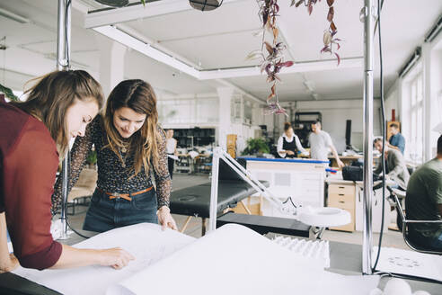 Unternehmerinnen diskutieren über Papier am Tisch in einem kreativen Büro - MASF14733