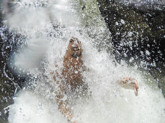 Selfie eines jungen Erwachsenen beim Baden unter dem Wasserfall eines Regenwaldflusses - CAVF69074