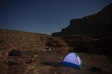 Tents illuminated by moonlight in a rugged desert environment at night - CAVF69124