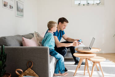 Vater und Sohn schauen sich zu Hause gemeinsam einen Laptop an - CAVF69163