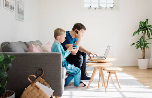 Father sat at home with his son on his mobile and laptop - CAVF69168