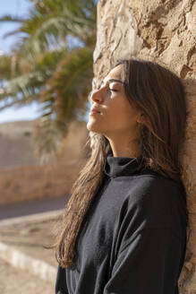 Portrait of young brunette woman with closed eyes leaning on a wall - AFVF04182