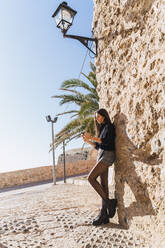 Junge brünette Frau benutzt Smartphone und lehnt sich an eine Wand - AFVF04183