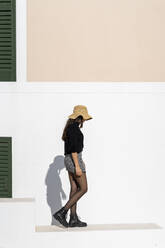 Junge brünette Frau mit Sonnenhut, die auf einer weißen Wand läuft - AFVF04187