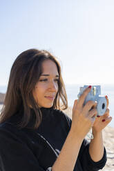 Porträt einer jungen brünetten Frau, die mit einer blauen Kamera fotografiert - AFVF04191