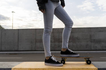 Beine einer Frau mit Skateboard, die auf einem Poller steht - GIOF07686