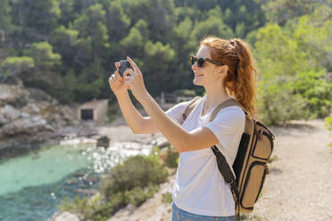 Redheaded woman standing on viewpoint and photographing with her smartphone - AFVF04198