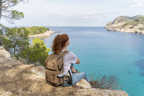 Rothaarige Frau sitzt auf einem Aussichtspunkt und schaut in die Ferne, Ibiza - AFVF04201