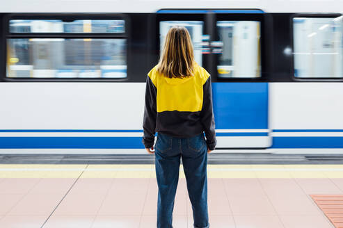 Rückansicht einer jungen Frau, die auf dem Bahnsteig einer U-Bahn-Station steht - JCMF00276