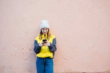 Young woman standing in front of a wall using smartphone - JCMF00280