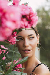 Porträt einer jungen Frau in einem Park mit rosa blühenden Blumen - AFVF04205