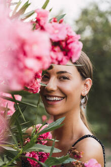 Porträt einer lachenden jungen Frau in einem Park mit rosa blühenden Blumen - AFVF04206