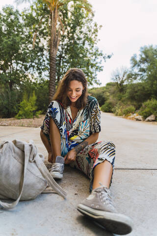 Laughing young woman sitting on slab in a park putting on shoe stock photo