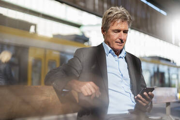 Mature businessman waiting at station platform using cell phone - DIGF08907