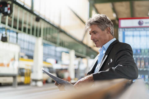 Älterer Geschäftsmann liest Zeitung auf dem Bahnsteig, lizenzfreies Stockfoto