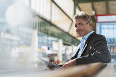 Smiling mature businessman with newspaper on station platform - DIGF08910