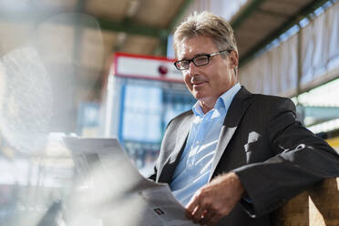 Mature businessman reading newspaper on station platform - DIGF08911