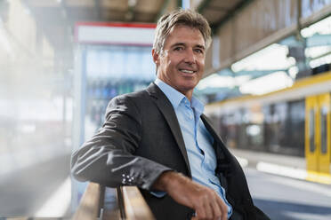 Portrait of smiling mature businessman waiting at station platform - DIGF08914