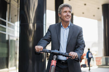 Mature businessman with e-scooter in the city - DIGF08920