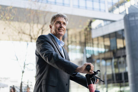 Älterer Geschäftsmann mit E-Scooter in der Stadt, lizenzfreies Stockfoto