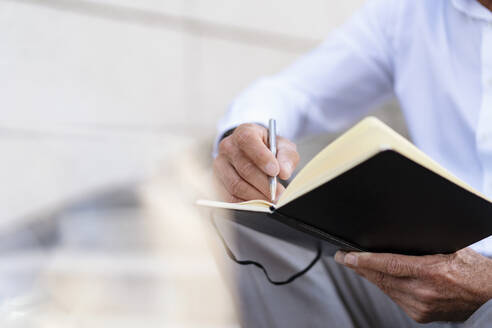 Nahaufnahme eines Geschäftsmannes auf einer Treppe sitzend mit einem Notizbuch - DIGF08951