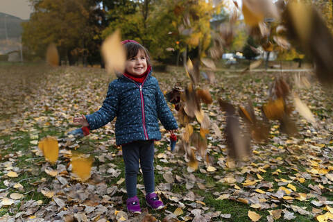 Kleines Mädchen spielt mit Herbstblättern im Freien, lizenzfreies Stockfoto