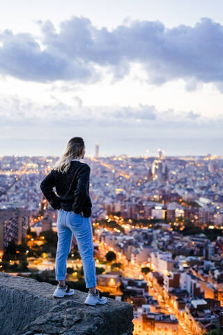 Rückansicht einer jungen Frau, die in der Morgendämmerung über der Stadt steht, Barcelona, Spanien, lizenzfreies Stockfoto