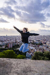 Unbekümmerte junge Frau, die bei Sonnenaufgang über die Stadt springt, Barcelona, Spanien - GIOF07702