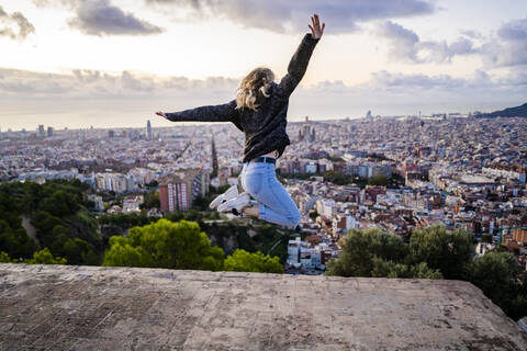 Unbekümmerte junge Frau, die bei Sonnenaufgang über die Stadt springt, Barcelona, Spanien, lizenzfreies Stockfoto