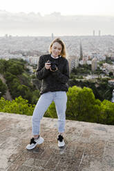 Junge Frau mit Kamera über der Stadt bei Sonnenaufgang, Barcelona, Spanien - GIOF07710