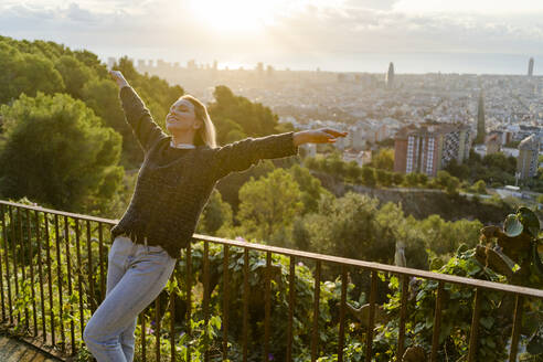 Unbeschwerte junge Frau, die bei Sonnenaufgang über der Stadt steht, Barcelona, Spanien - GIOF07712