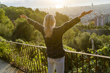 Rear view of carefree young woman standing above the city at sunrise, Barcelona, Spain - GIOF07713