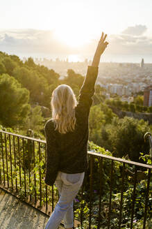 Rückansicht einer unbekümmerten jungen Frau, die bei Sonnenaufgang über der Stadt steht, Barcelona, Spanien - GIOF07714