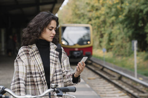 Frau mit Fahrrad und Mobiltelefon auf dem Bahnsteig einer U-Bahn-Station, Berlin, Deutschland, lizenzfreies Stockfoto