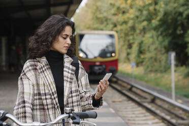 Woman with bicycle and cell phone on an underground station platform, Berlin, Germany - AHSF01197